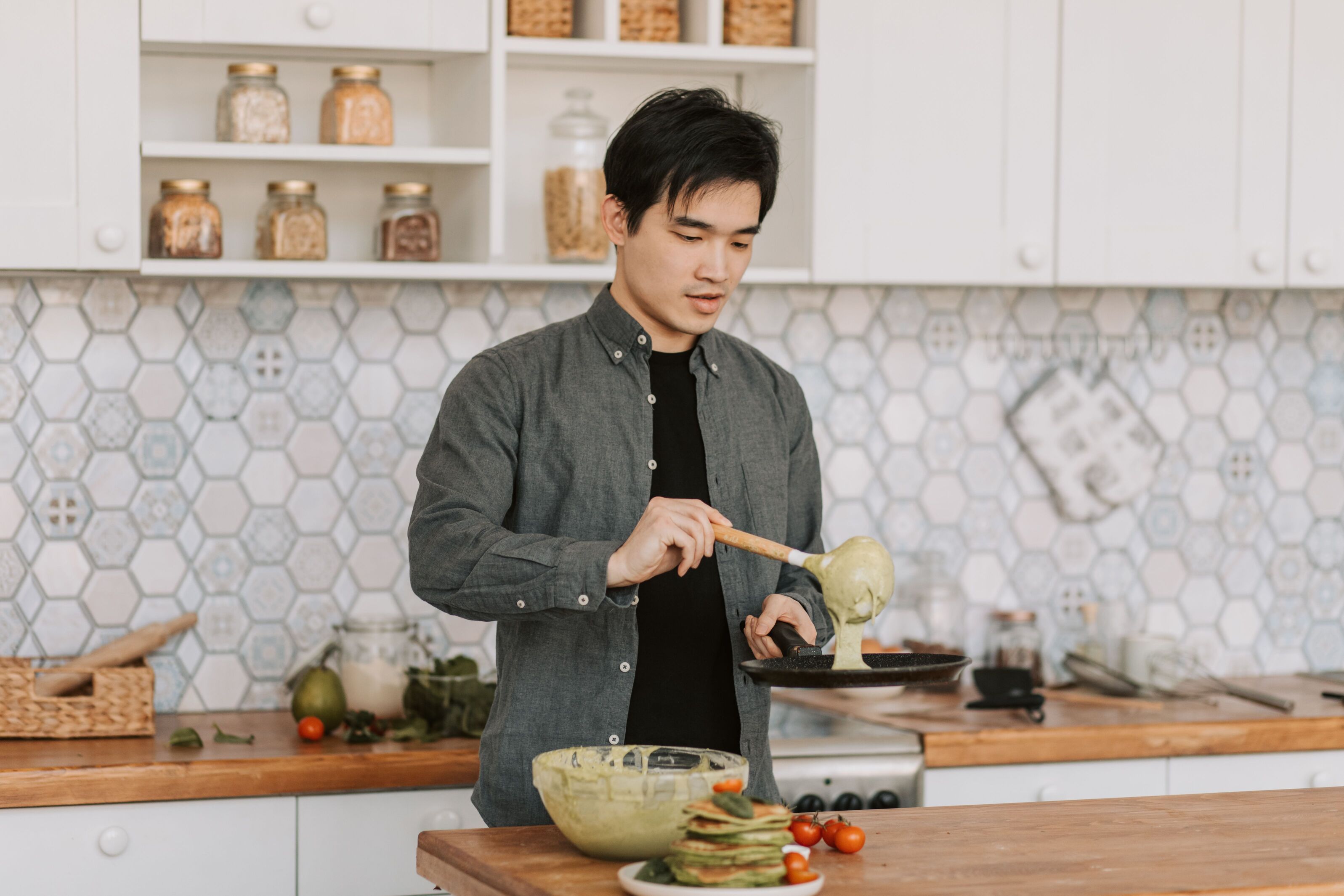 A man cooking at a bright home kitchen counter with bowls of vegetables